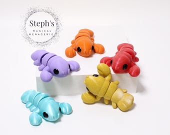 May include: A selection of brightly coloured lobster figurines in orange, red, yellow, purple, and teal. Each lobster has segmented bodies and black eyes. The image includes the text "Steph's Magical Menagerie" in a circular design.