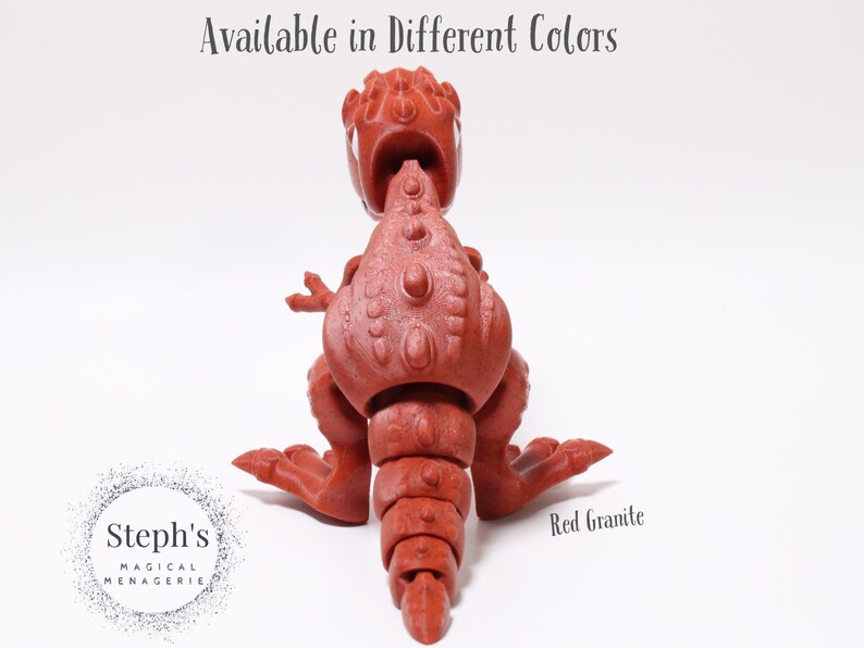 May include: Red granite dinosaur toy with articulated limbs. The dinosaur is sitting on a white surface. Available in different colours.