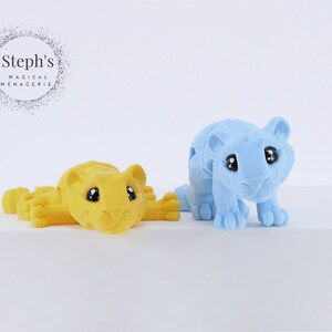 May include: Two small toy tigers, one yellow and one light blue, with black eyes. The tigers are posed in a playful manner.