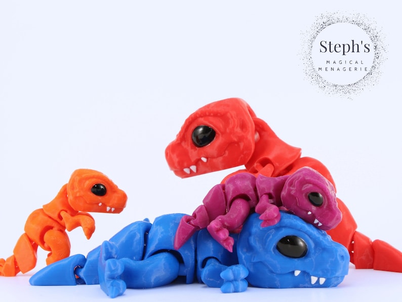 May include: A collection of articulated dragon figures in various colors: orange, red, blue, and purple. The dragons have large black eyes and are posed in a playful arrangement. The image includes the text "Steph's MAGICAL MENAGERIE".