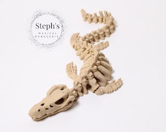Può includere: Statuetta di scheletro di alligatore beige. La statuetta mostra dettagli di costole, vertebre e cranio. Il testo "Steph's MAGICAL MENAGERIE" è in un cerchio in alto a sinistra. Su sfondo bianco.
