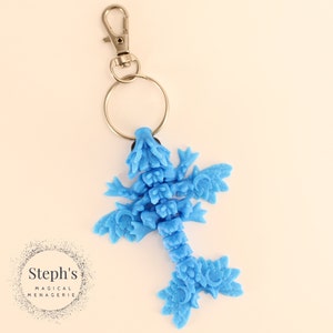 May include: A light blue dragon keychain with a silver key ring and clasp. The dragon is made of plastic and has a detailed design.