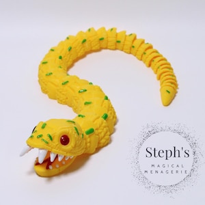 May include: A yellow rubber snake toy with green spots and a toothy, red-eyed head.