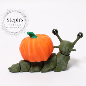 May include: A novelty green snail ornament with a vibrant orange pumpkin shell. The snail has large, cartoonish eyes and is set against a white backdrop. The text "Steph's MAGICAL MENAGERIE" is in the upper left.