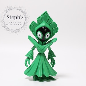 May include: A green figurine of a stylized creature with a leaf-like headpiece and a flowing skirt. The figure has a black face with large white eyes. The text "Steph's MAGICAL MENAGERIE" is in a circle in the background.