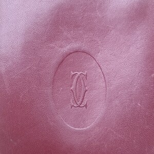 May include: A close-up of a burgundy leather surface with a raised oval-shaped logo. The logo is a stylized letter 'C' with a curved line through the center. The logo is embossed into the leather.