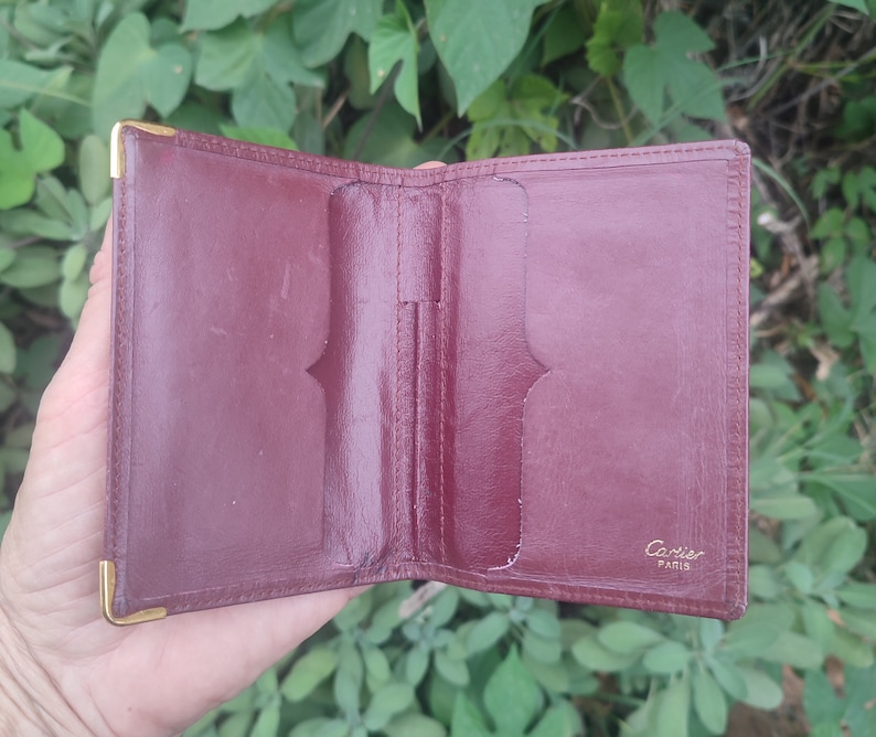 May include: A burgundy leather wallet with gold accents and the words 'Cartier Paris' embossed on the front.