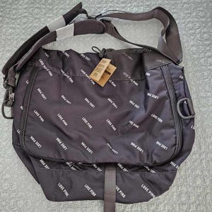 May include: A black messenger bag with a white "Love Pink" pattern. The bag has a zippered closure and a strap that can be adjusted. The bag is made of a durable nylon material.