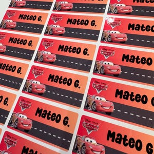 May include: Rectangular stickers featuring the Disney Pixar Cars character Lightning McQueen. Each sticker has a red and orange gradient background, a black road design, and the name "Mateo G." printed in black.