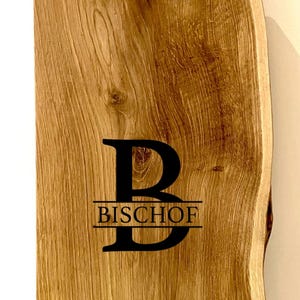 Puede incluir: Una tabla de cortar de madera grande, rectangular, con un borde vivo y un asa. La tabla est&aacute; hecha de madera marr&oacute;n claro con un acabado natural. La tabla tiene la letra "B" y el nombre "BISCHOF" grabados.