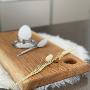 Puede incluir: Una tabla de servir de madera con un corte redondo y una ramita de flores secas. La tabla es de madera marr&oacute;n claro y tiene un acabado natural.