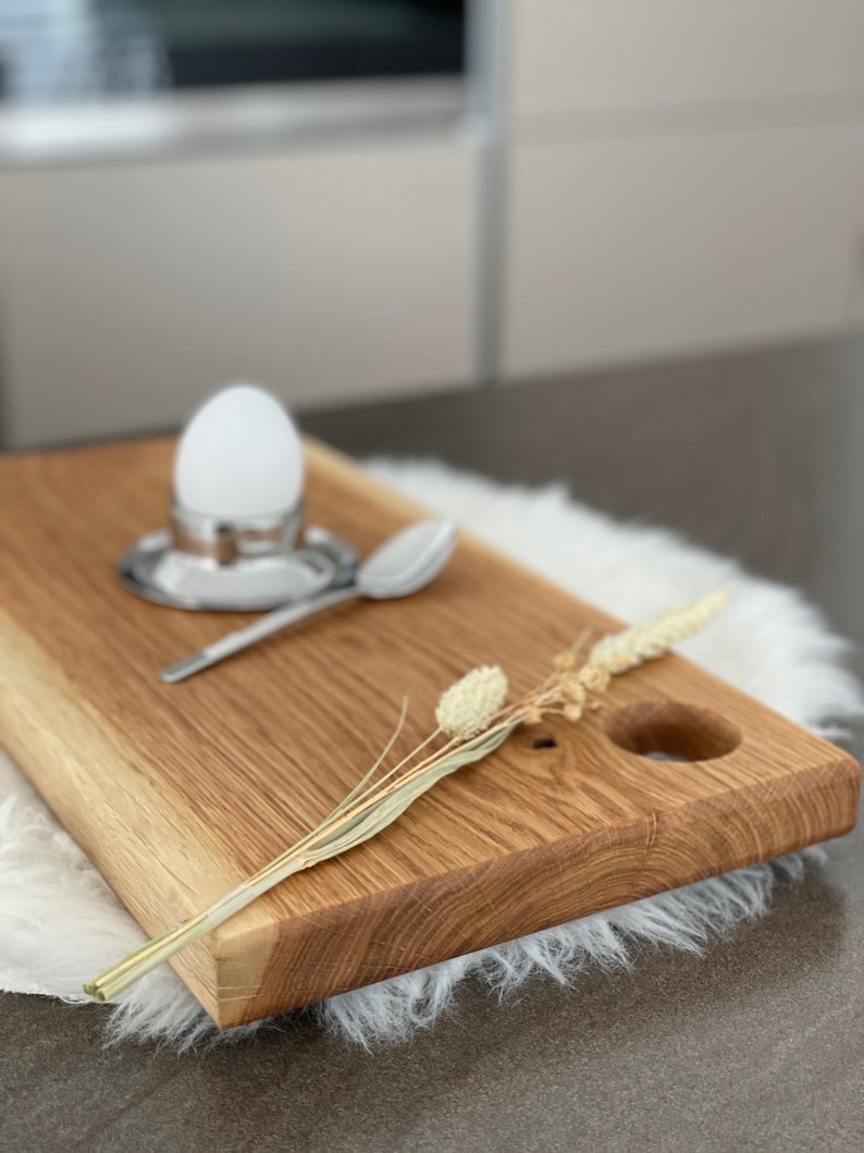 Puede incluir: Una tabla de servir de madera con un corte redondo y una ramita de flores secas. La tabla es de madera marr&oacute;n claro y tiene un acabado natural.