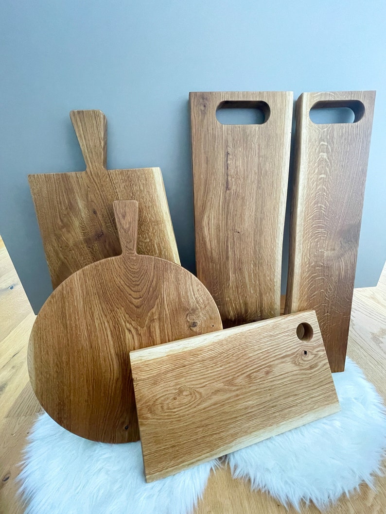 Puede incluir: Cinco tablas de cortar de madera de diferentes tama&ntilde;os y formas. Las tablas son de madera marr&oacute;n claro con un acabado natural. Algunas de las tablas tienen asas, mientras que otras tienen agujeros para colgar.