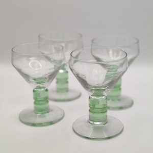 May include: Set of four clear glass shot glasses with green glass stems. The stems are decorated with a geometric pattern.