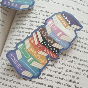 Puede incluir: Una pila de libros coloridos con varios patrones y dise&ntilde;os, incluyendo estrellas, lunas y flores. Los libros est&aacute;n dispuestos en una pila, con el libro superior azul y el libro inferior morado.