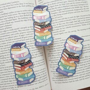 Puede incluir: Una pila de libros de pegatinas coloridos con un esquema de colores arco&iacute;ris. Los libros de pegatinas est&aacute;n dispuestos en una pila con las espinas hacia afuera. Los libros de pegatinas est&aacute;n sobre un fondo blanco.