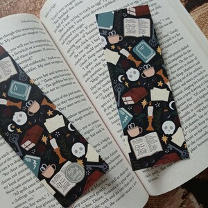 May include: Two black and white bookmark designs featuring a repeating pattern of skulls, keys, books, candles, and teacups. The text "Ash & Bookie" is printed on the bookmarks.