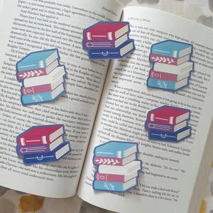 May include: A selection of book-shaped stickers with red, blue, and white spines, placed on an open book. The stickers have different designs, some with decorative details. The background is a book page.