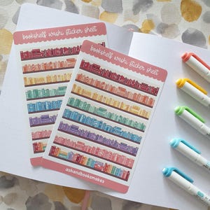 May include: Two sticker sheets with a bookshelf design. Each sticker sheet has a pink border and the text "bookshelf washi sticker sheet". The bookshelves are filled with colorful books. The text "ashandbooksmakes" is at the bottom of one sticker sheet. Four colorful pens are in the background.
