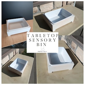 May include: A white tabletop sensory bin with a white plastic insert, set in a white wooden frame. The bin is rectangular with a slightly raised edge. The text "TABLETOP SENSORY BIN" is displayed in the center of the image.