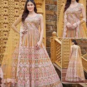 May include: A long, flowing, golden-brown gown with intricate pink and white embroidery. The gown has a sleeveless design and a scoop neckline. The gown is paired with a sheer, golden-brown dupatta.