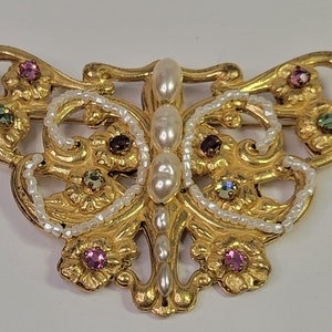 Può includere: Un fermaglio a forma di farfalla in oro con dettagli in perle e strass colorati.