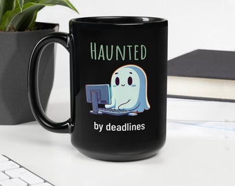 Op de afbeelding: Zwarte koffiemok met een wit spookontwerp. Het spook zit aan een computer en de tekst "HAUNTED by deadlines" staat onder het spook.