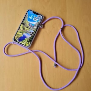 May include: A clear phone case with a purple phone strap. The phone screen displays the time 16:04.