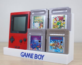 May include: A white Game Boy stand with a red Game Boy and four gray Game Boy cartridges. The cartridges are labeled "Kirby's Dream Land", "Yoshi", "Tetris", and "Super Mario Land".