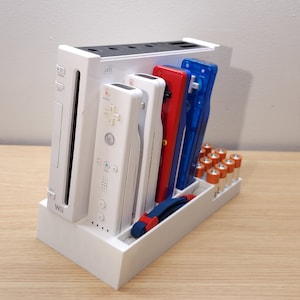 Puede incluir: Consola Wii U blanca con dos mandos Wii blancos, un cartucho de juego rojo y azul y un compartimento para bater&iacute;as. La consola est&aacute; sobre una superficie de madera.