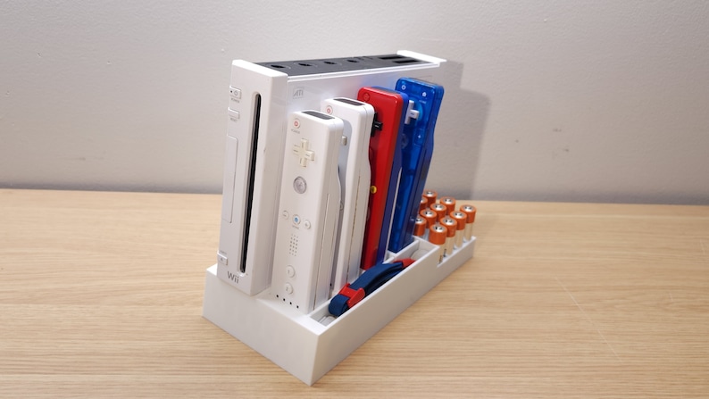 Puede incluir: Consola Wii U blanca con dos mandos Wii blancos, un cartucho de juego rojo y azul y un compartimento para bater&iacute;as. La consola est&aacute; sobre una superficie de madera.