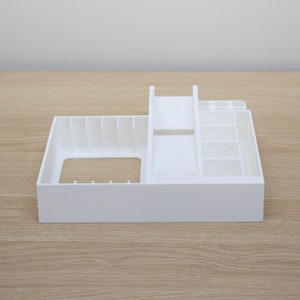 Puede incluir: Organizador de pl&aacute;stico blanco con m&uacute;ltiples compartimentos para guardar objetos peque&ntilde;os. El organizador tiene un compartimento rectangular grande en la parte delantera y un compartimento m&aacute;s peque&ntilde;o con divisores verticales en la parte trasera.