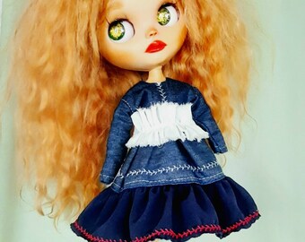 May include: A doll with long, curly, reddish-blonde hair wearing a blue denim dress with a white ruffle and yellow shoes.