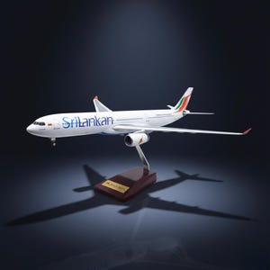 May include: A white model airplane with the word "Srilankan" in blue lettering on the side. The model has red and green accents on the tail and is mounted on a wooden base. The model airplane is a collectible item.