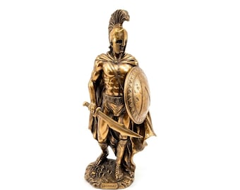 May include: A bronze-colored statue of a Spartan warrior wearing a plumed helmet, a cape, and greaves. The figure holds a sword in the right hand and a round shield in the left hand. A plaque at the base of the statue features the text LEONIDAS.