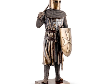 May include: A bronze-toned knight figurine standing on a rectangular base. The knight wears a cylindrical helmet, chainmail armor, and a tunic featuring a silver cross. A shield with a Maltese cross emblem is held in the left hand, while a weapon rests over the right shoulder.