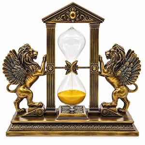 May include: A bronze-colored hourglass set within a rectangular frame featuring two winged lions on either side. The structure includes a pediment top and a base with intricate detailing. The clear glass hourglass contains golden sand.