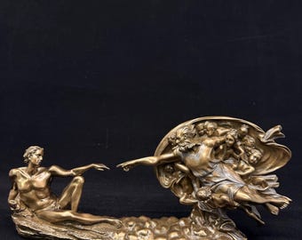 May include: A bronze-colored sculpture depicting Michelangelo's "The Creation of Adam." The sculpture features two figures, one reclining and the other surrounded by figures, with outstretched arms. The sculpture is on a black background.