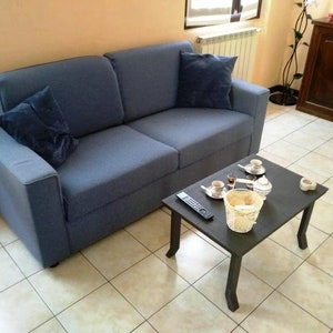 May include: A blue fabric sofa with two pillows sits in a living room with a small black coffee table and a wooden cabinet in the background.