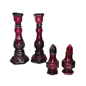 Pode incluir: Conjunto de quatro castiçais e saleiro e pimenteiro de vidro vermelho rubi. Os castiçais são altos e finos com um design decorativo. O saleiro e o pimenteiro são menores e redondos com um design semelhante.