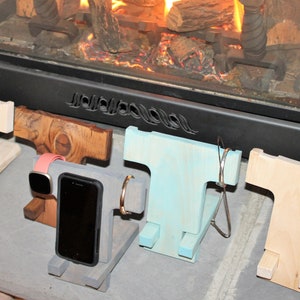 May include: Four wooden phone stands in different colors and styles. The stands are designed to hold a phone, watch, and other small items. The stands are arranged in a row on a gray surface.