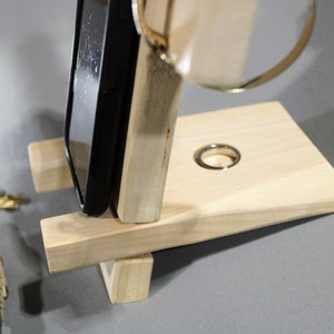 May include: A wooden phone stand with a ring holder. The stand is made of light wood and has a simple design. The phone is not included.