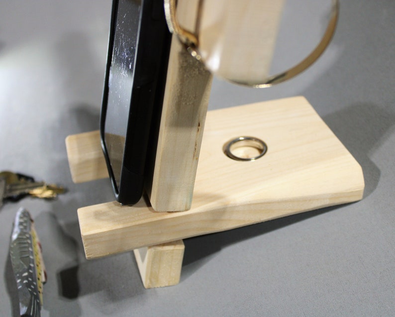 May include: A wooden phone stand with a ring holder. The stand is made of light wood and has a simple design. The phone is not included.