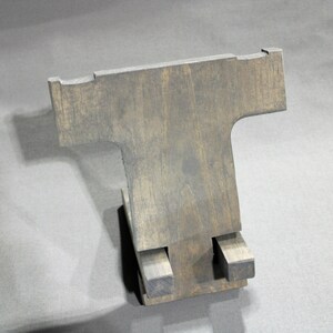 May include: A wooden phone stand with a T-shaped design. The stand is made of dark wood and has a rustic finish.