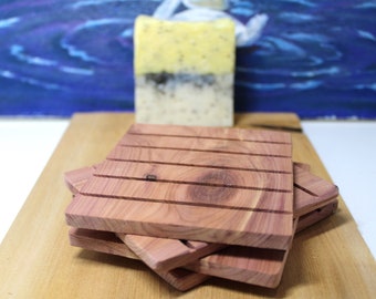 May include: A set of four cedarwood soap savers, stacked on top of each other. The savers are made of natural cedarwood and have a reddish-brown color. They are designed to help extend the life of soap bars by allowing them to dry out between uses.