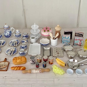 May include: A selection of miniature kitchen items, including a blue and white tea set, plates, cookware, baking supplies, and food items. Miniature cookbooks, a cake, and a rolling pin are also present. The items are arranged on a light-coloured surface.