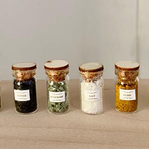 May include: Eight small glass spice jars with cork lids, each containing a different spice. Labels on the jars identify the contents as paprika, parsley, pepper, rosemary, salt, curry, clover, and cinnamon.