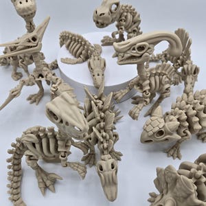 May include: A collection of beige dinosaur skeleton models, including a Pterodactyl, Triceratops, and other prehistoric creatures. The articulated figures are arranged on a white surface, showcasing their detailed bone structures. These models are ideal for educational purposes or as unique decorative items.