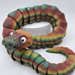May include: A colorful segmented snake toy with a textured surface and a cartoon-like face. The snake is made of a flexible material and is curled into a circle.