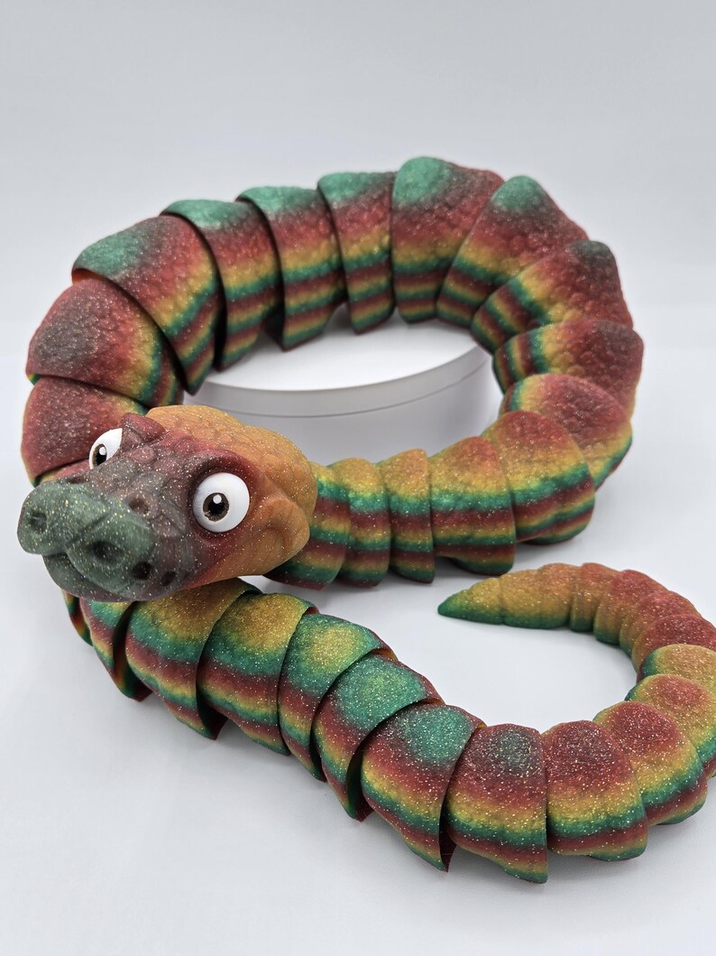 May include: A colourful segmented snake toy with a textured surface and a cartoon-like face. The snake is made of a flexible material and is curled into a circle.